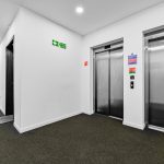 Modern hallway with elevators and fire exit sign.