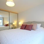 Modern bedroom with double bed and mirrored wardrobe.