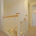 Carpeted hallway with stair railing and doors