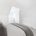 Minimalist white bedroom with grey bedding and window.