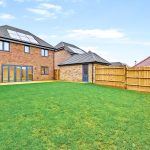 Modern house with solar panels and fenced garden.
