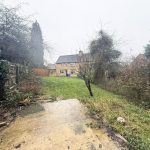 Overgrown garden with a small brick house.
