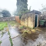 Overgrown garden with shed and wheelie bins.