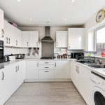 Modern white kitchen with appliances and wooden flooring.