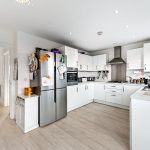 Modern white kitchen with appliances and wooden floor.