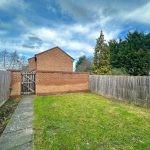 Fenced green garden with brick house and trees.