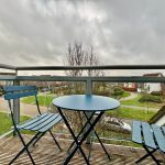 Balcony view with table and chairs, cloudy sky.