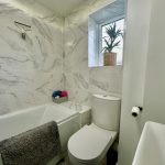 Modern bathroom with marble tiles and plant.