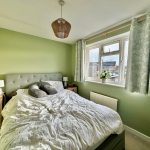 Cosy bedroom with green walls and large window.