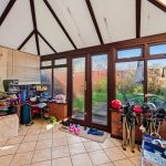 Cluttered conservatory with garden view and chairs.