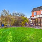 Back garden with patio and conservatory in sunlight.