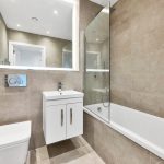 Modern bathroom with beige tiles and white fixtures.