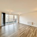 Spacious empty room with wooden flooring and balcony.