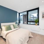 Modern bedroom with blue accent wall and large window.