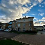 Residential street with cars and cloudy sky.