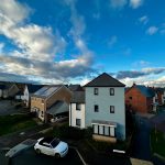 Residential street with houses under cloudy blue sky.