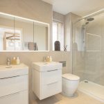 Modern beige bathroom with shower and double sinks.