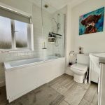 Modern bathroom with bath, shower, and artwork.